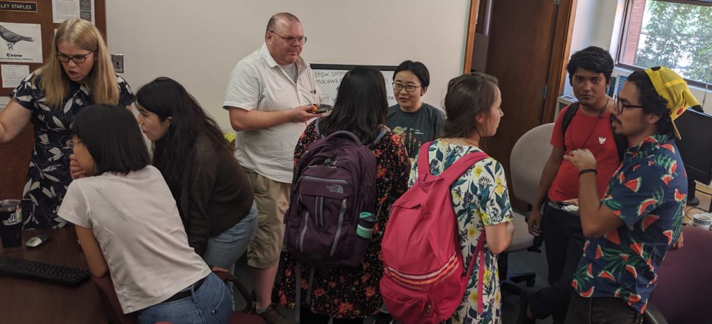 Gathering of people standing in a small office. At left, Shelley Staples demonstrates the Crow interface. 