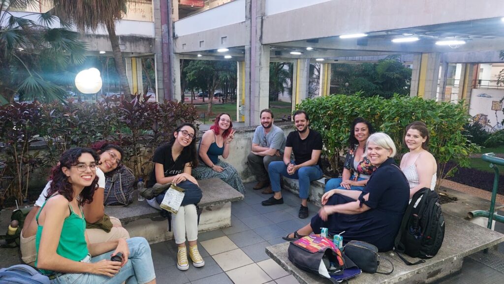 Post-course chat with Dr. Staples, faculty, and students in a courtyard at UFMG. They all smile and look at the camera while sitting on close concrete benches.